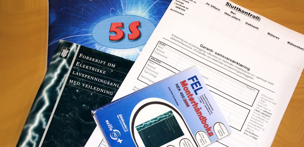 Lovtekster, montørhåndbok og sluttkontrollskjema ligger på et bord. Foto.