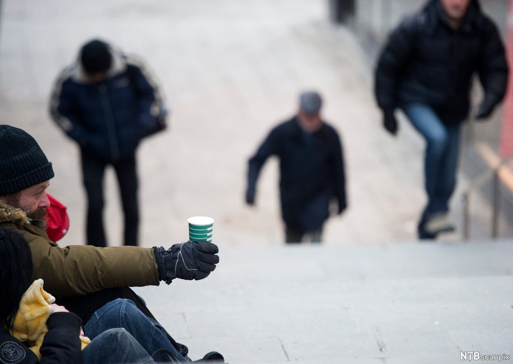 En tigger på gaten holder fram en pappkopp mot forbipasserende. Foto. 
