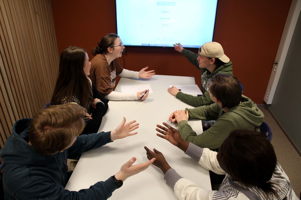 Møterom med seks unge personer som diskuterer. I bakgrunnen en storskjerm. Foto.