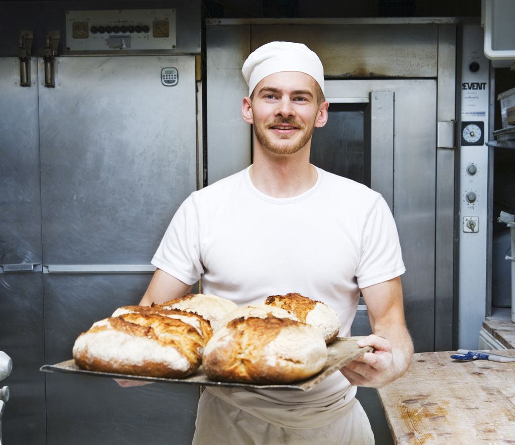 En baker i et bakeri holdet et brett nystekte brød. Foto.