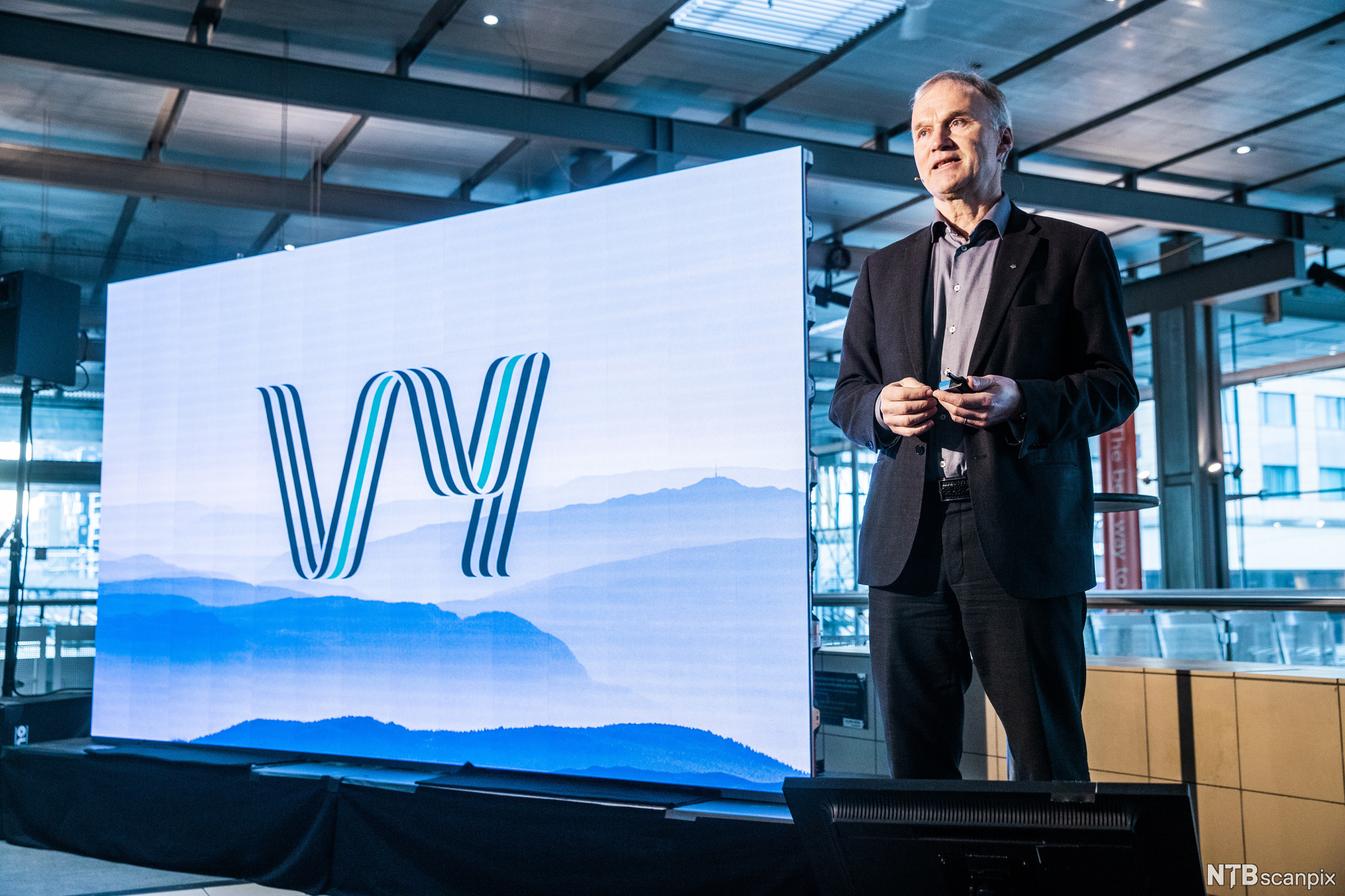 Mann ved siden av tavle med logoen til Vy. Foto.