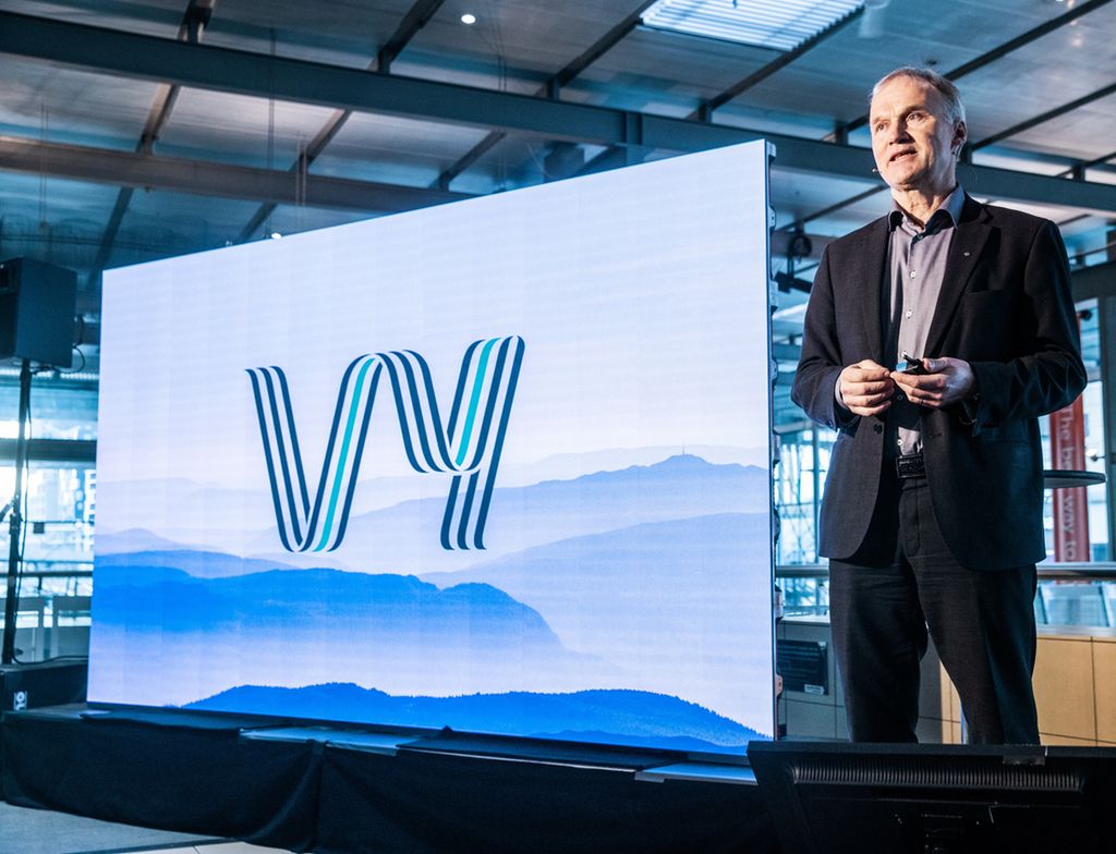 Mann ved siden av tavle med logoen til Vy. Foto.