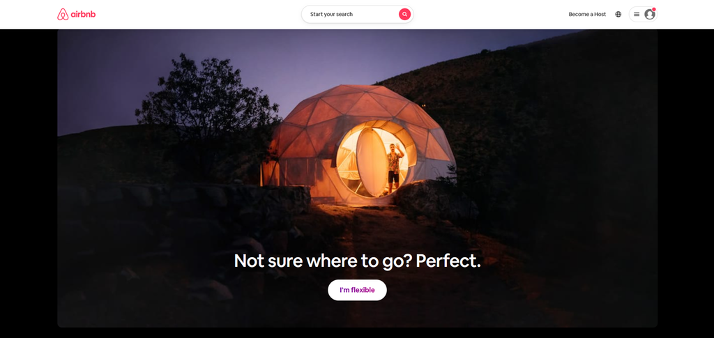Nettsida til Airbnb som viser et opplyst telt i et mørkt landskap. Under teltet står teksten Not sure where to go? Perfect. I'm flexible. Øverst på bildet står det airbnb, og ved siden av er det et søkefelt hvor det står Start your search. Skjermutklipp.