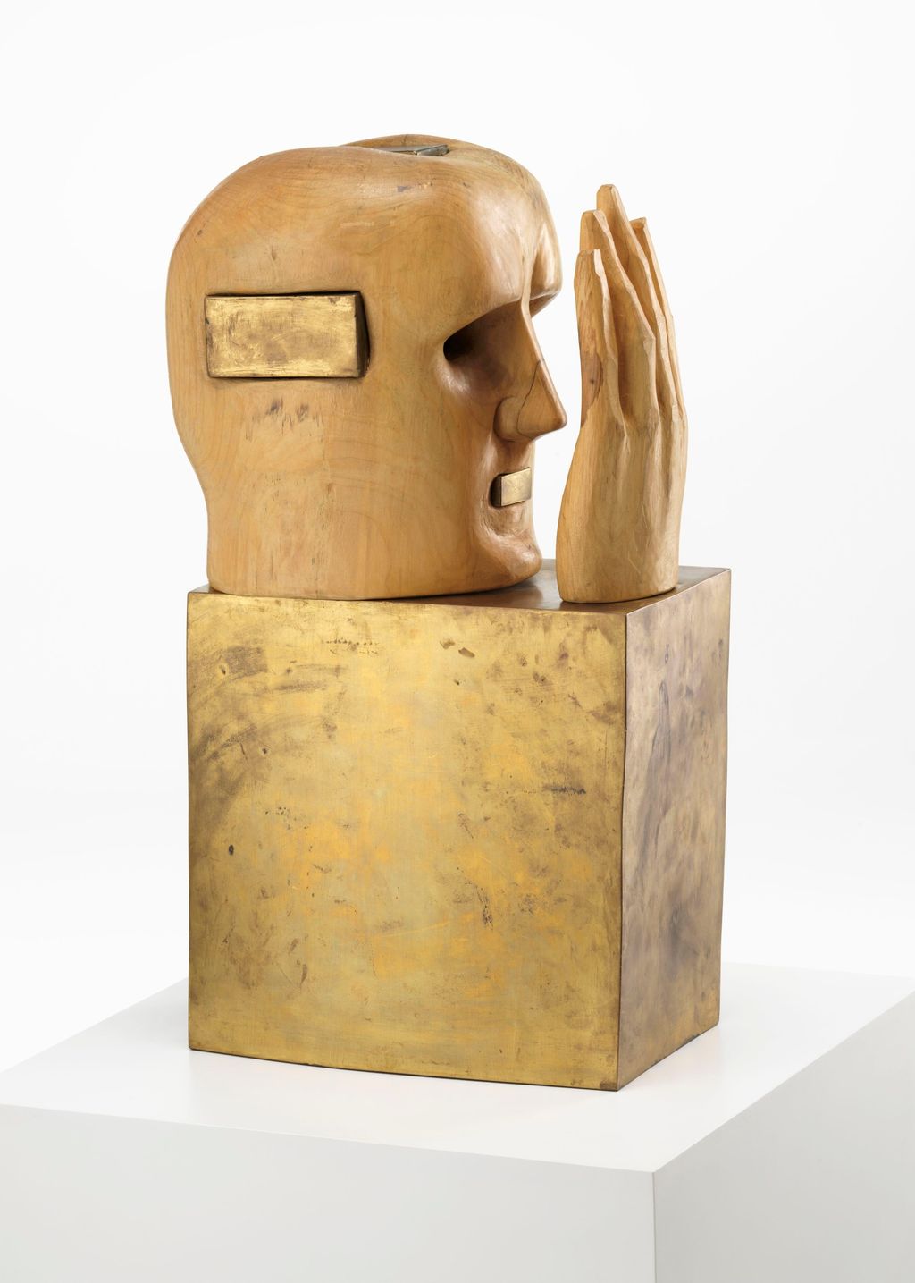 Treskulptur av et hode som ser inn i ei hånd. Foto.