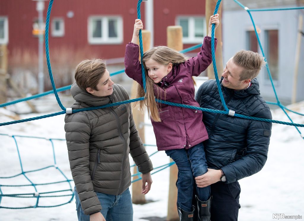 To unge menn og ei jente. Jenta klatrer i tau. De unge mennene ser på henne og smiler. Foto.