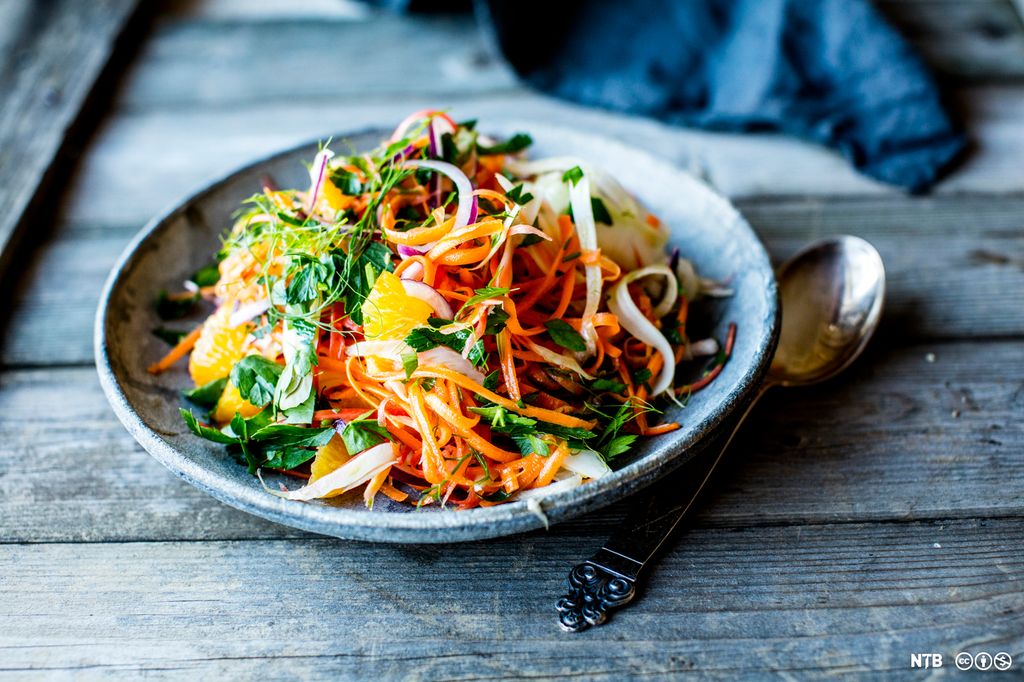 En skål med råkostsalat av blant annet strimlet gulrot, rødløk, appelsin og urter. Foto.