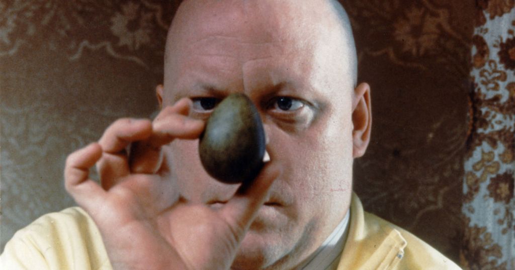 Mann i gul skjorte ser på et grønt egg. Bilde fra filmen Eggs. Foto.