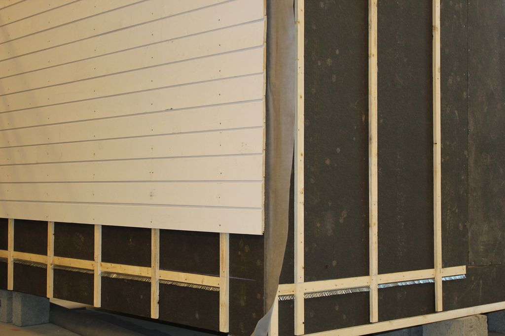 Liggende bordkledning på vegg med asfaltplater og lekter. Foto.