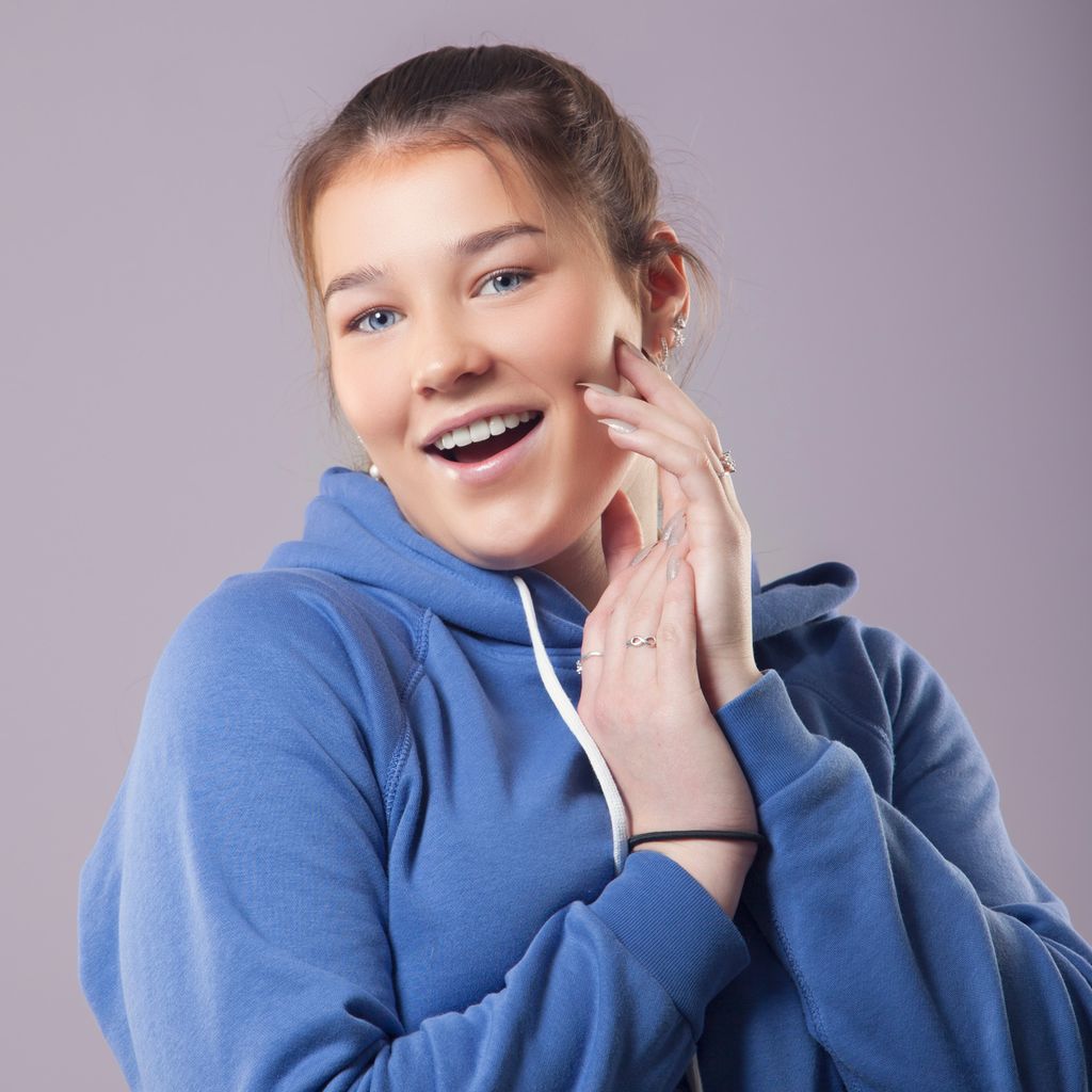 Happy teenage girl in a blue hoodie posing for the camera. Photo.