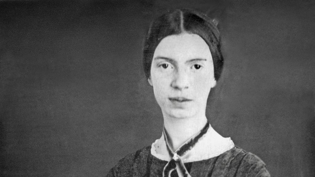 Photo: Portrait of Emily Dickinson. We see a woman with large brown eyes and dark hair. She has a ribbon tied around her neck. 