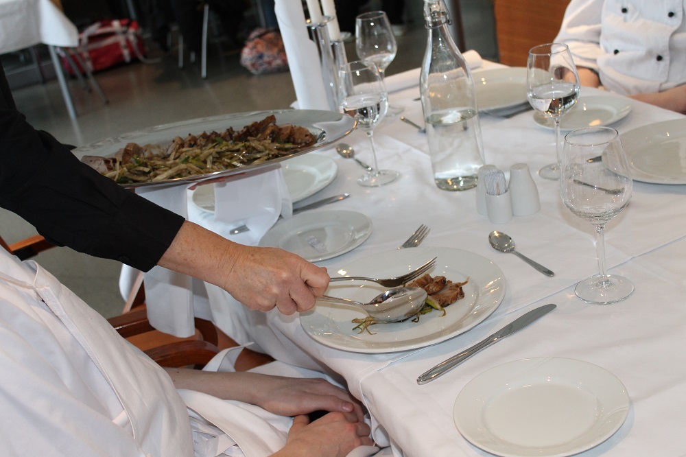 Servitør legger mat på gjestens tallerken. Foto.