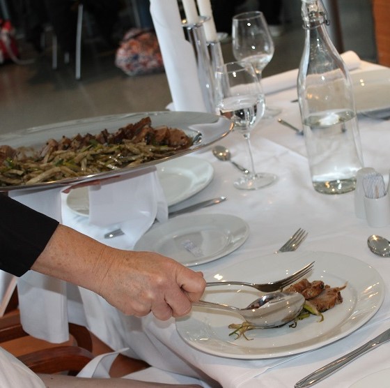 Servitør legg kjøttskiver frå eit fat over på tallerkenen til gjesten. Foto.