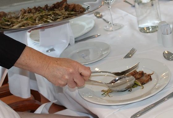 Servitør legg kjøttskiver frå eit fat over på tallerkenen til gjesten. Foto.