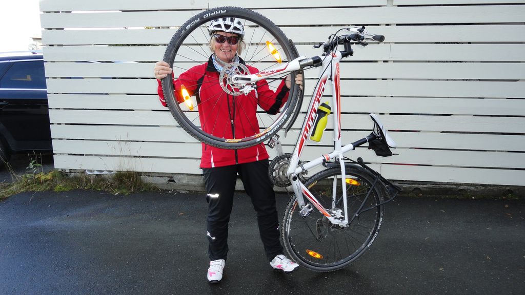 Wenche held opp sykkelen sin og ser gjennom framhjulet. Foto.