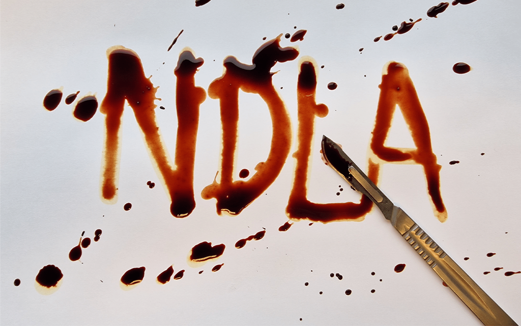 Bokstavene n, d, l og a, skrevet i en farge som minner om størknet blod. Et skalpell er plassert delvis over skriften. Bladet  på skalpellen har samme farge som teksten. Foto.