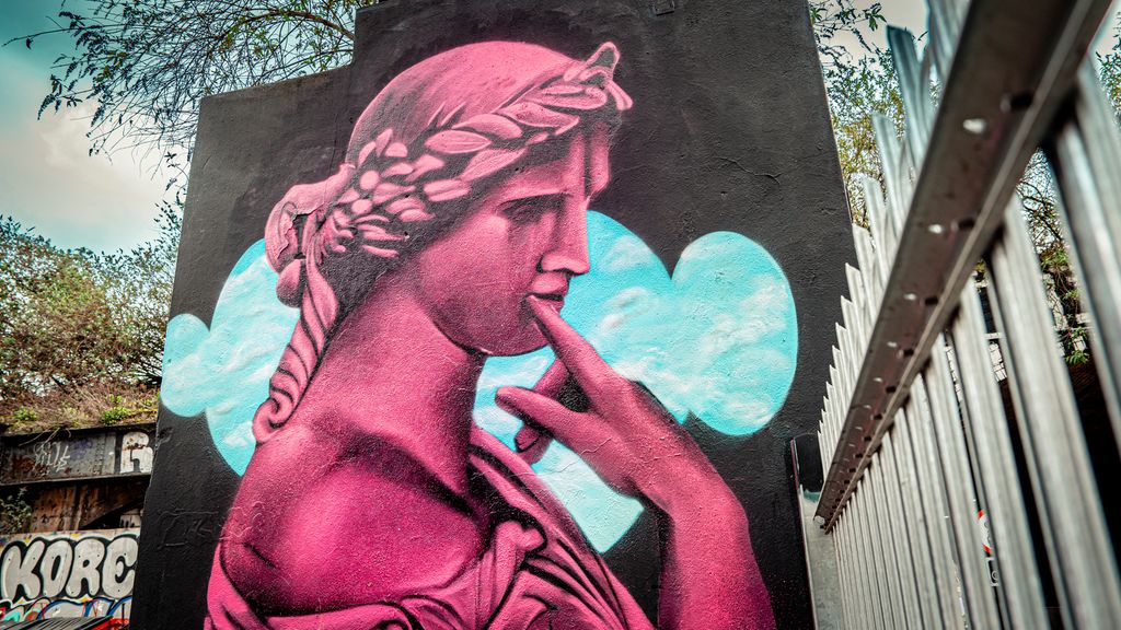 Gatekunst av David Speed som viser et grafittbilde av en rosa greskinspirert statue på en murvegg. Foto.