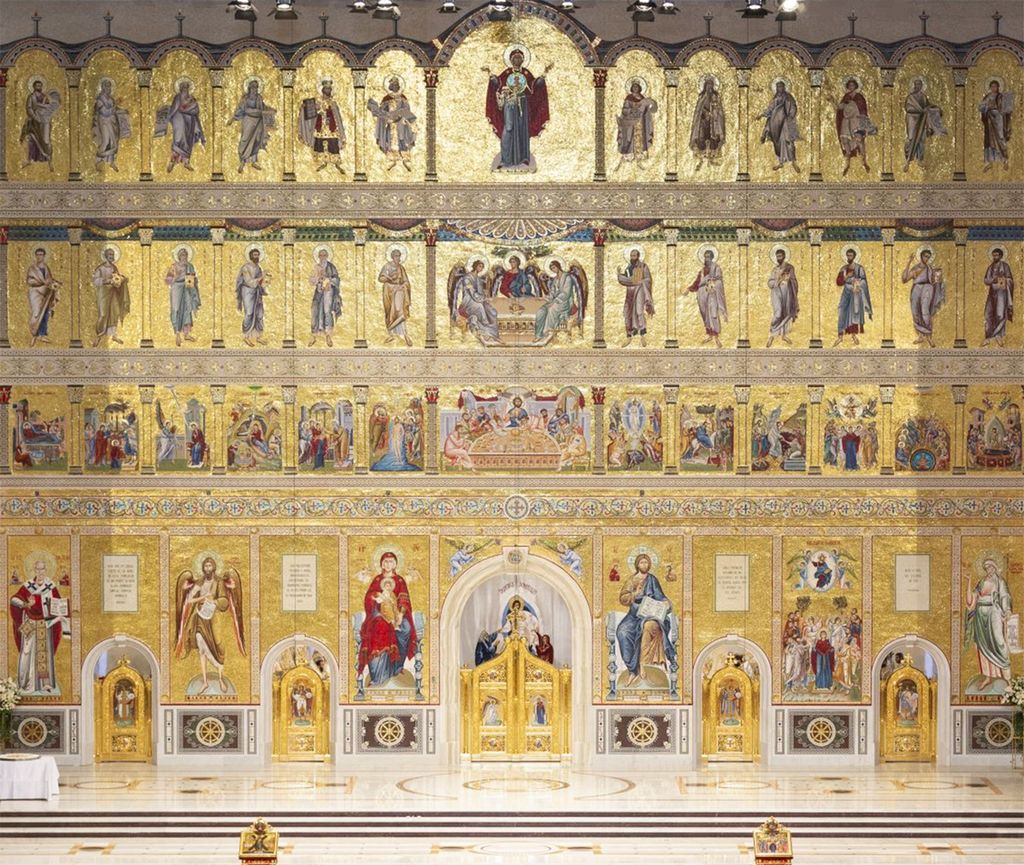 Gullbelagt vegg med ulike avbildninger av mennesker med glorie. Veggen har fem porter. Foto.