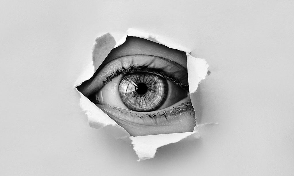 Øye ser gjennom et hull i et papir. Foto.