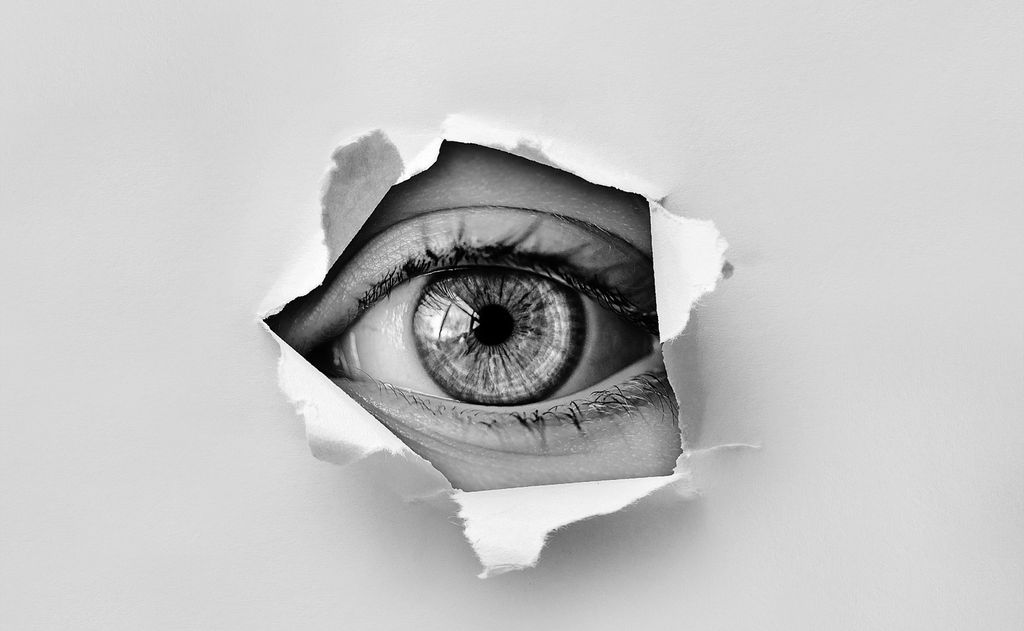 Øye ser gjennom et hull i et papir. Foto.