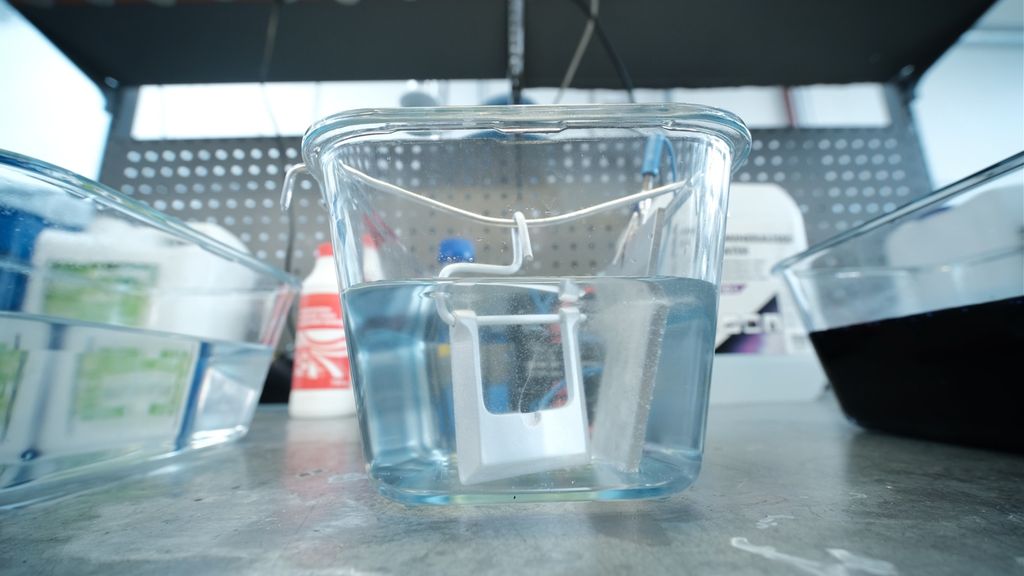 Blank beltespenne som er dyppa i en glassbeholder med væske. Foto.