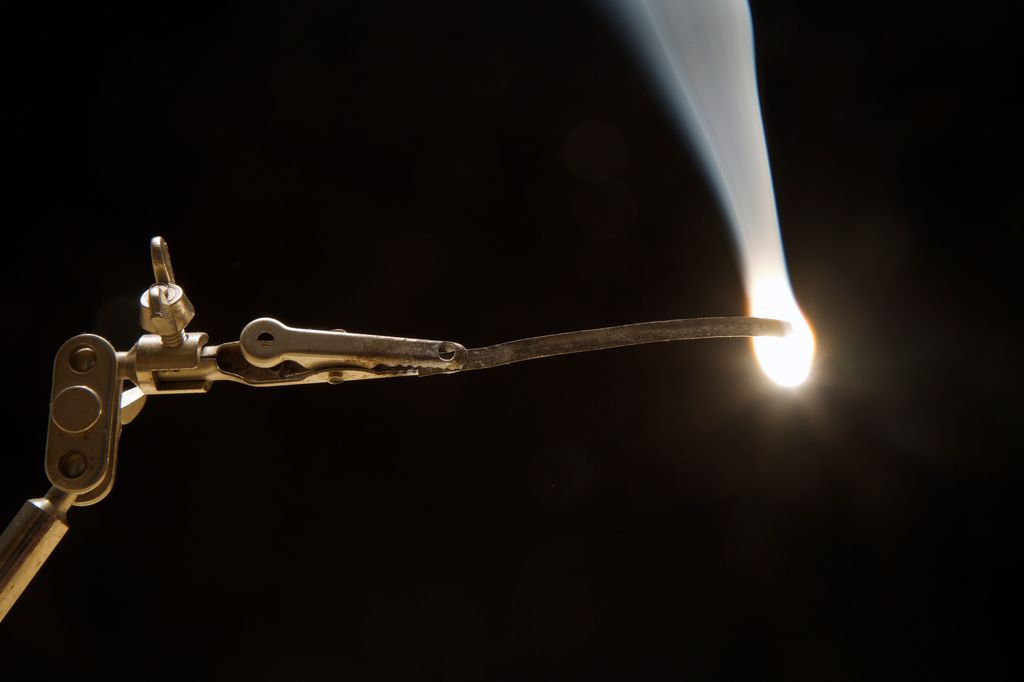 Ei metallklemme held noko som brenn med eit kvitt lys. Foto.