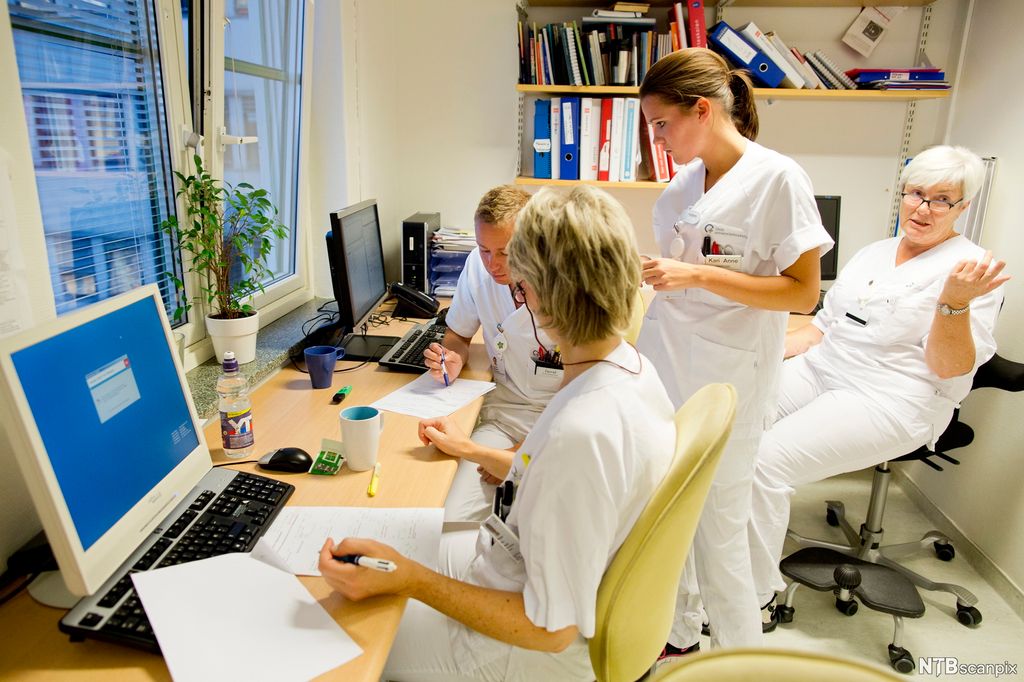 Helsepersonell som diskuterer på et kontor, to av dem noterer på ark. Foto.