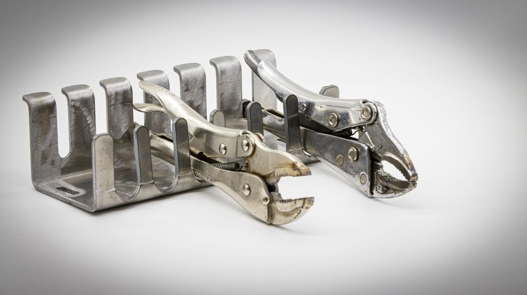 Metallstativ som ligger på et bord. To tenger ligger i stativet. Foto.