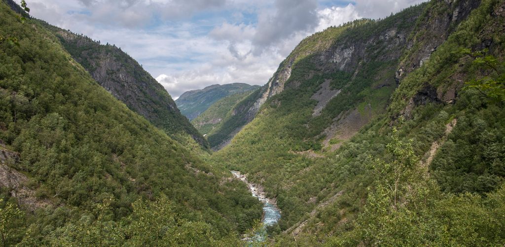 Ei elv som renn på botnen av ein V-forma, skogkledd dal. Foto.