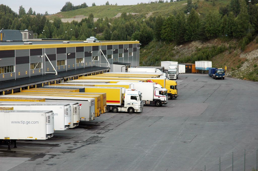 På bildet ser vi mange lastebiler som leverer og henter varer ved en godsterminal. Foto.
