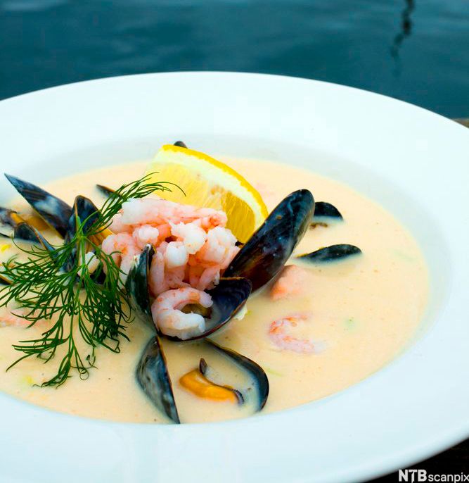 En skål med fiskesuppe som er garnert med reker, blåskjell, en sitronbåt og litt dill. Foto.