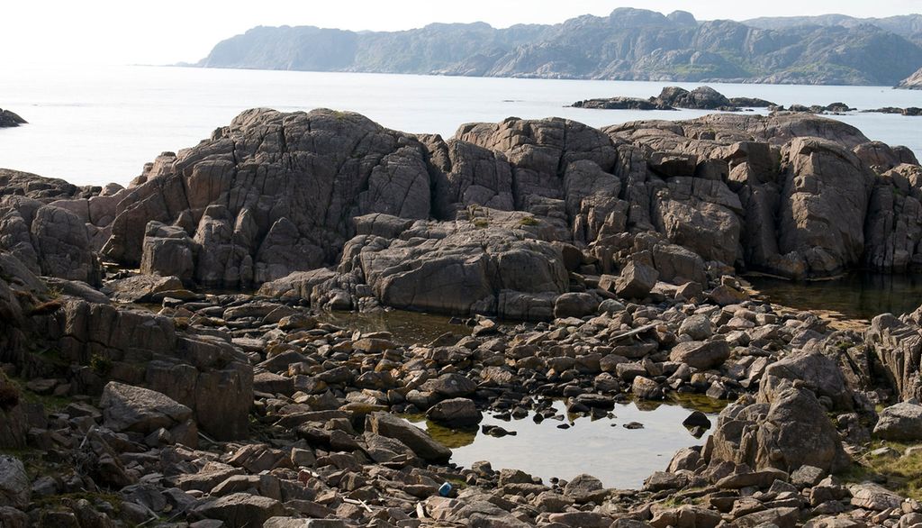 Mellom steinar i vasskanten er det ein stor fjørepytt. Bakom steinane er det ope hav. Foto