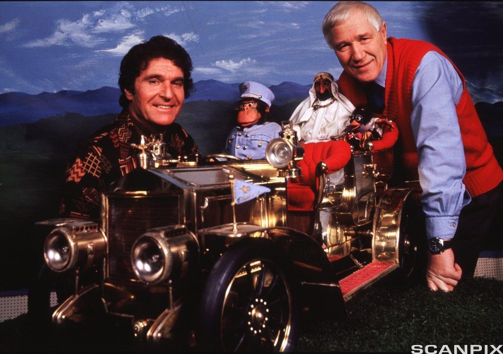Forfatter Kjell Aukrust og filmprodusent Ivo Caprino står rundt en stor modell av dene blanke og gylne racerbilen Il Tempo Gigante. I førersetet sitter den store apen Emanuel Desperados i blå uniform, og i passasjersetet sitter den hvitkledde sjeiken Ben Redic Fy Fazan og fuglen Solan, kledd i skinnjakke med pelskrage. Foto.