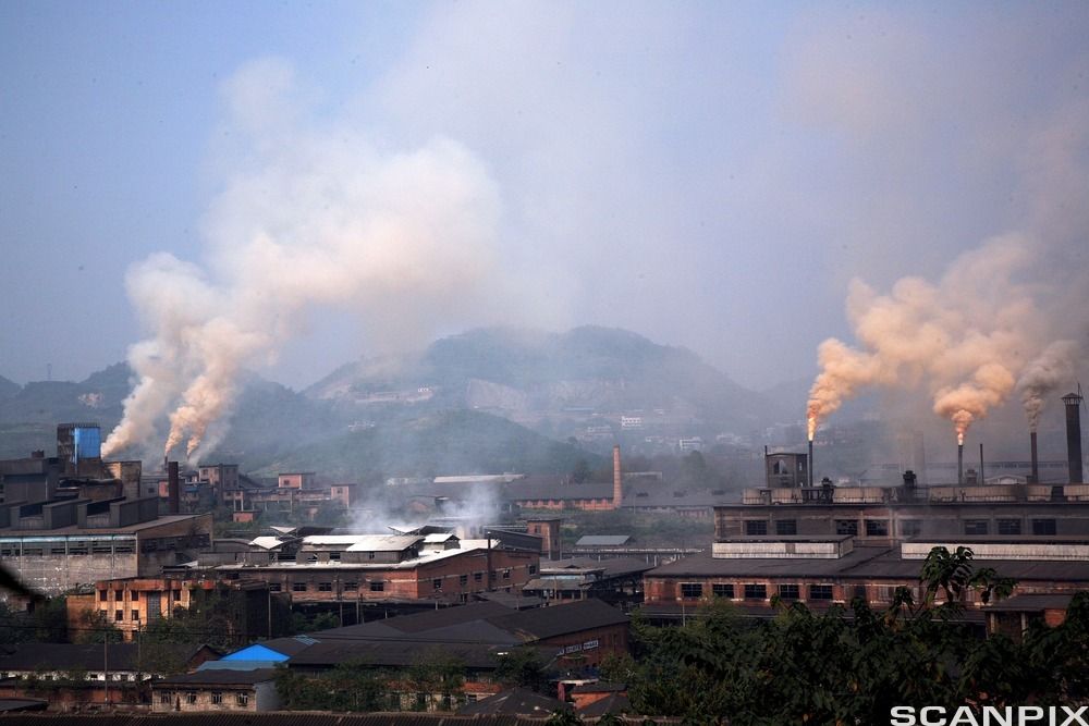 Område med industribygg med mange piper som slipper ut store mengder røyk. Lufta er uklar. Foto.