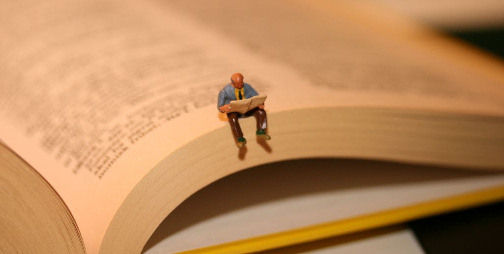 Miniature of a man reading is placed on the edge of a book. Photo.