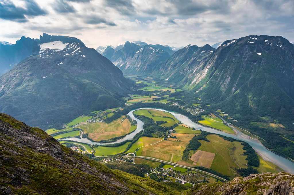 Bratte fjell på kvar si side av ein dal i bakgrunnen og ei svingete elv i forgrunnen. Foto.