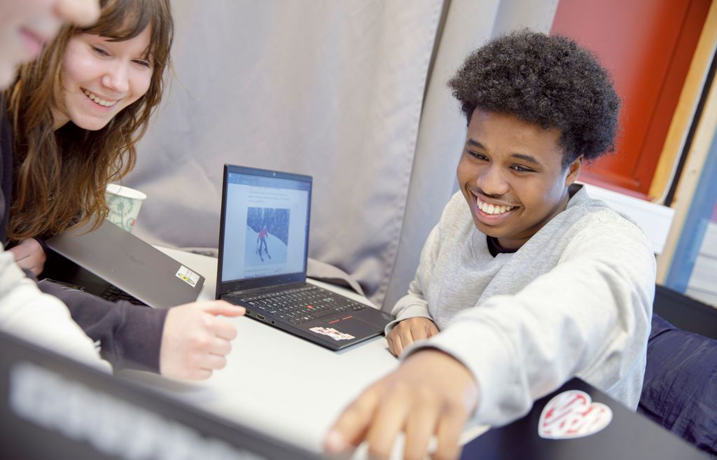 Smilende elever arbeider sammen med pc-er. Foto.