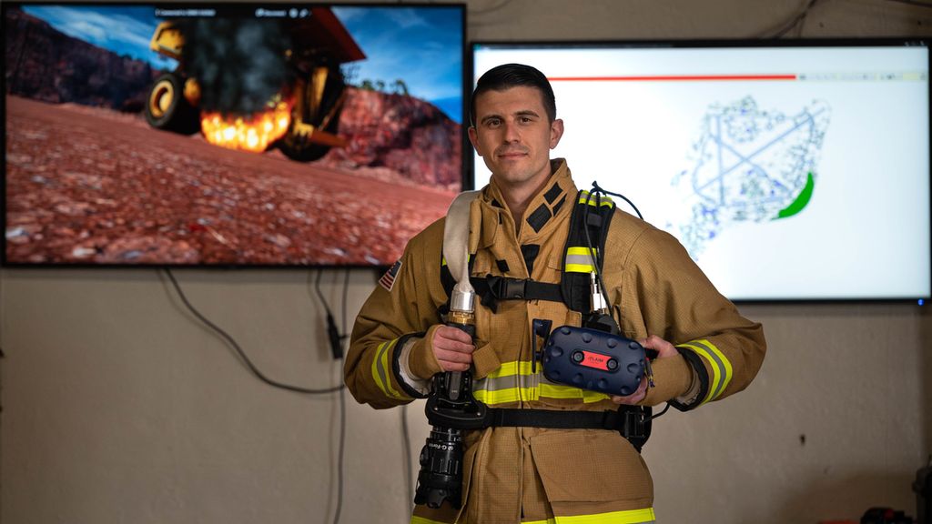 Brannkonstabel holder VR-briller og en digital brannslokker foran en tv-skjerm. Foto.