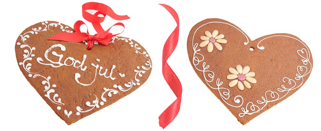 To peparkakehjarte som er fint dekorerte med melisglasur. Det eine har ein dekorativ bord, teksten God jul og raudt silkeband gjennom eit hol. Det andre har to blomstrar av skålda mandlar og ein samanhengande, dekorativ melisbord rundt kanten. Foto.