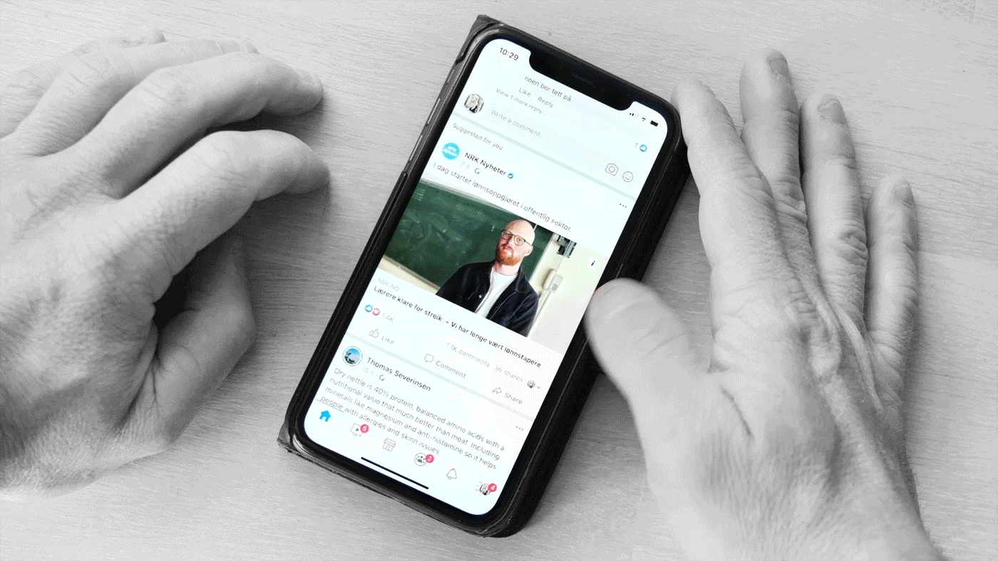 En "cinemagraph" av to hender og en mobil. Den høyre tommelen skroller på mobilen. Bare mobilskjermen har farger, resten er i svart-hvitt. Foto.