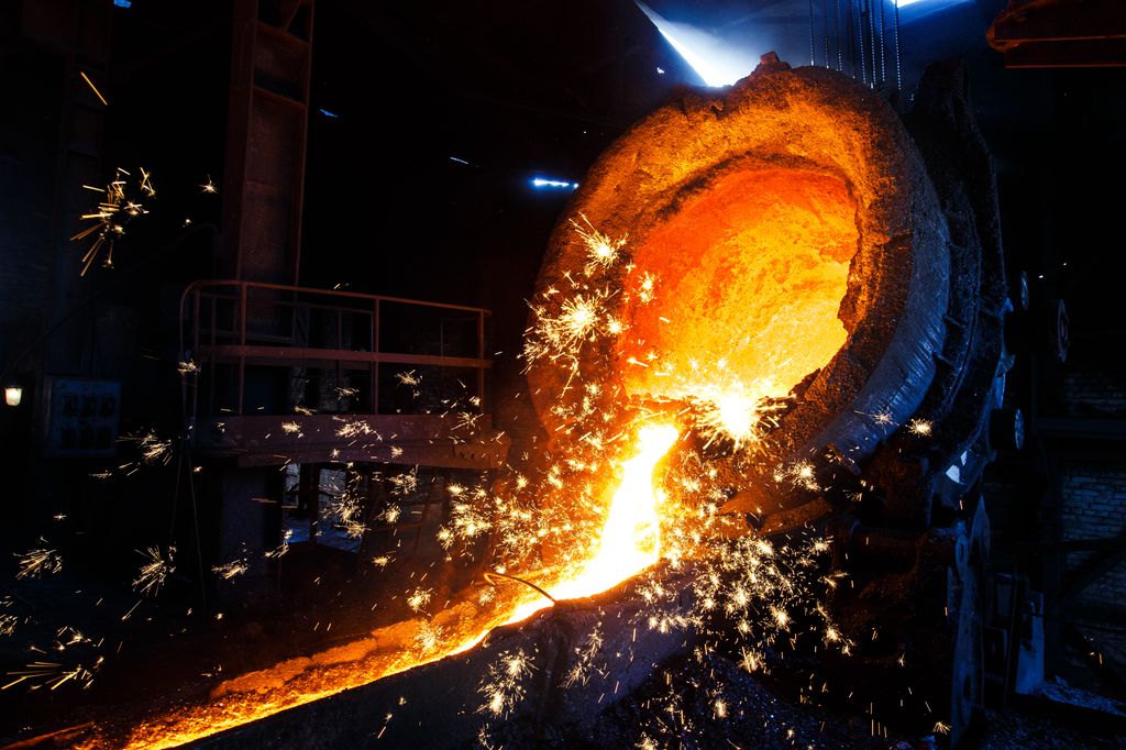 Smeltet metall som renner ut av en smeltedigel. Det gnistrer fra smeltebadet. Foto.