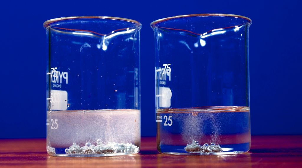 Sink i løsninger av saltsyre med ulik konsentrasjon i 2 kolber. Foto.