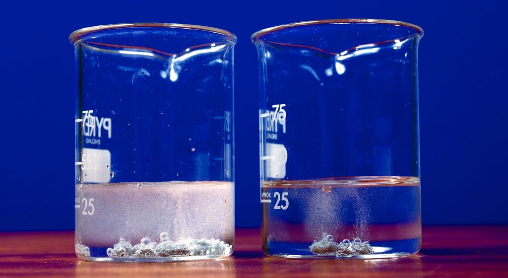 Sink i løysningar av saltsyre med ulik konsentrasjon i 2 kolbar. Foto.