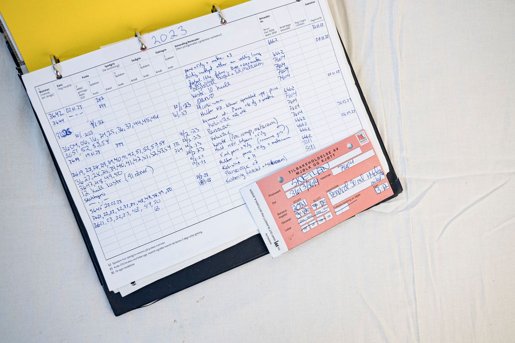 Ett av flere ark i en perm som viser dyrlegebehandlinger i et grisefjøs. Oppå arket ligger det en lapp om tilbakeholdelse av mjølk og kjøtt. Foto.