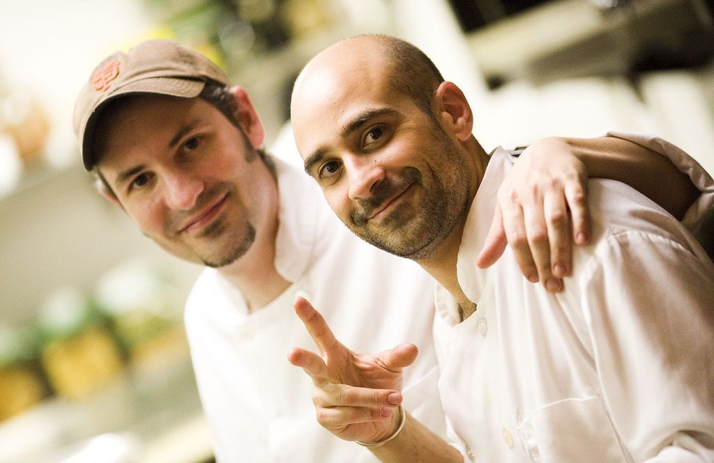 To glade kokker holder rundt hverandre på et kjøkken. Foto.