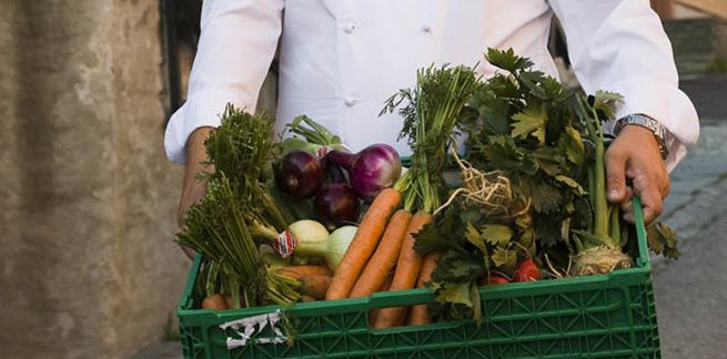 En person holder en kasse med grønnsaker. Foto.