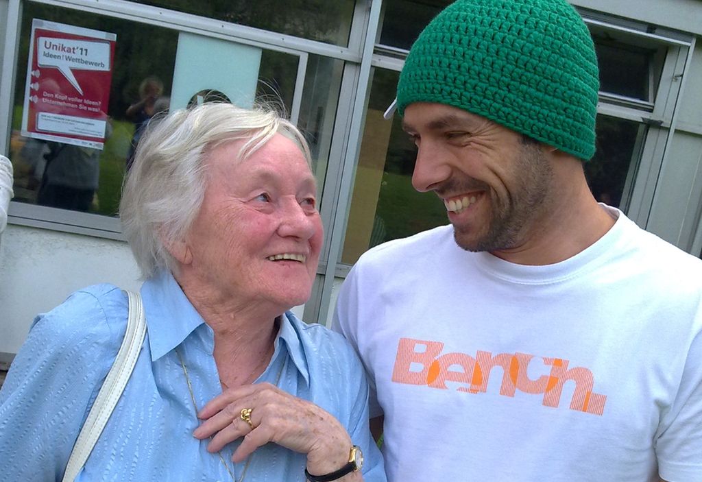 Gammel dame og ung mann som ser på hverandre og smiler inderlig til hverandre. Foto.