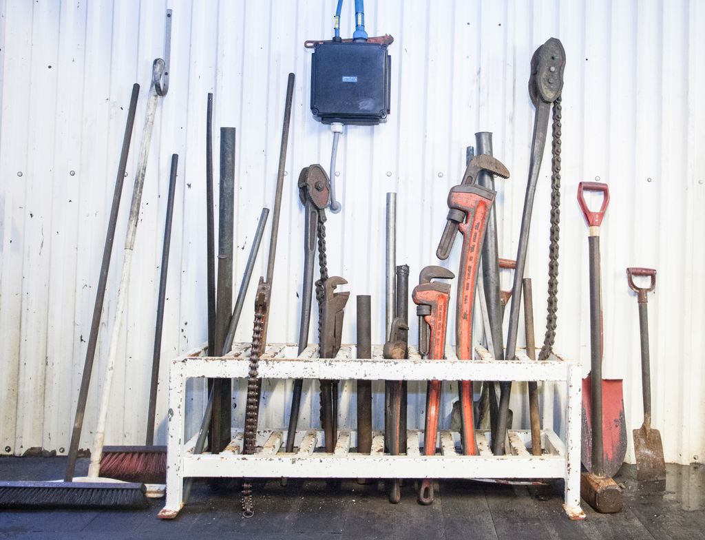 Forskjellige rørtenger stablet sammen med feiekoster og annet håndverktøy. Foto.