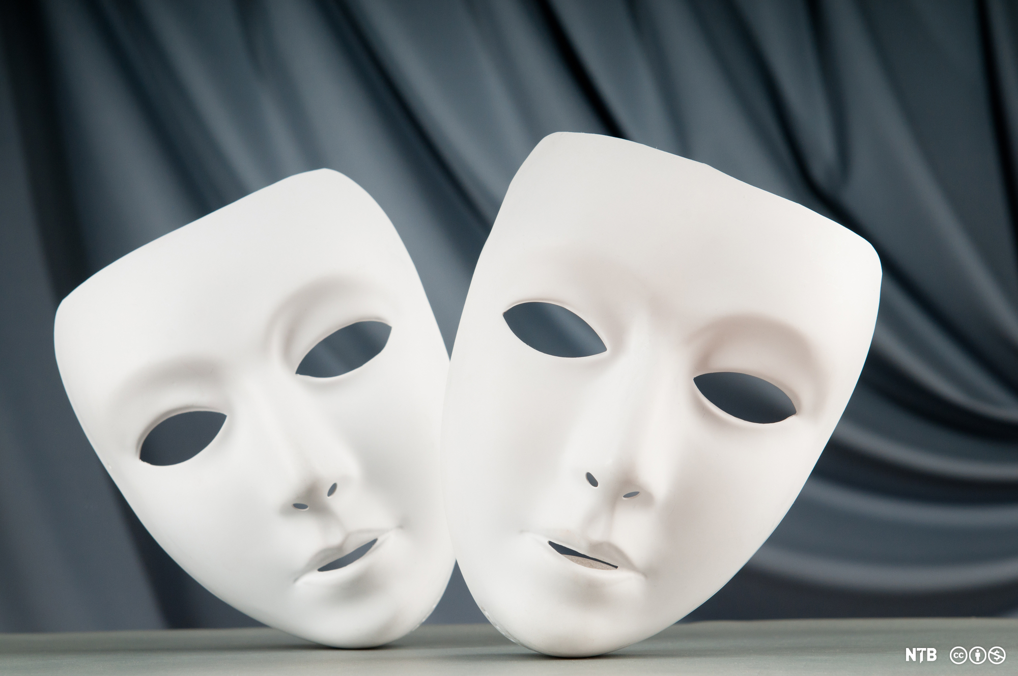 Theatre masks, two white masks with no expression, against a black background.  Photo.