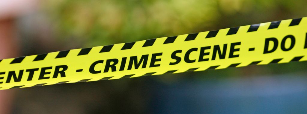 A black and yellow barricade tape reading 'Crime Scene'. Photo.