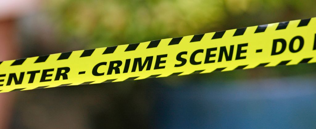 A black and yellow barricade tape reading 'Crime Scene'. Photo.